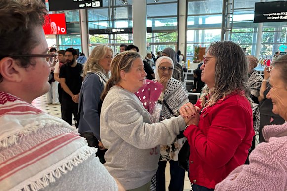 Flotilla activist Helen O’Sullivan (centre) arrives in Brisbane on Monday morning, greeted by about 20 family members and friends including Liam Parry (left), the first person charged under new Queensland hate speech laws. 