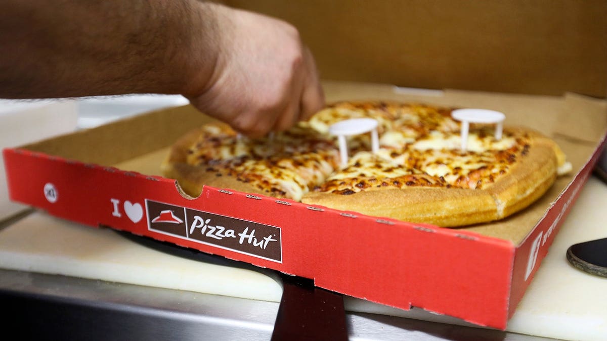 Employee placing plastic box supports around freshly cooked pizza in Pizza Hut kitchen.