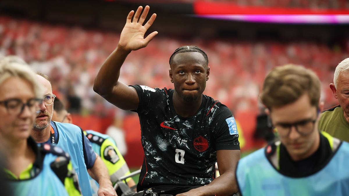 Ismael Kone of Canada waving to crowd while being stretched off soccer field.