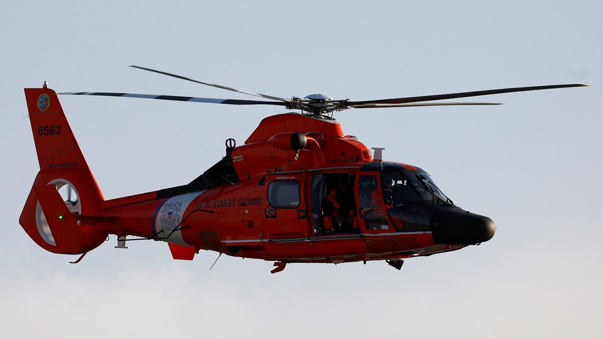 A U.S. Coast Guard MH-65 Dolphin helicopter flying along the San Diego coastline.
