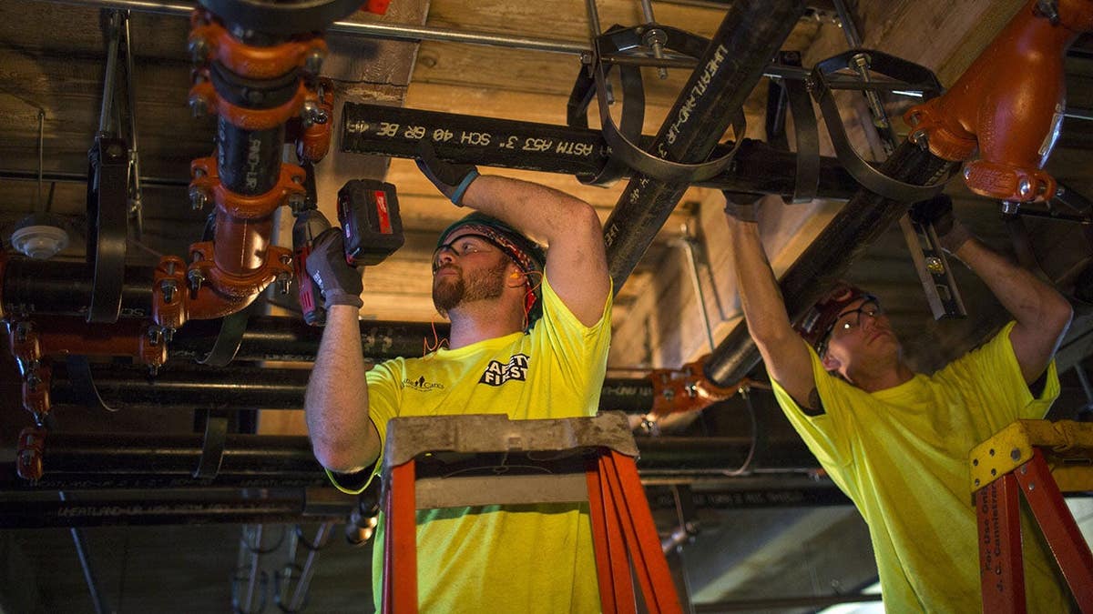 Plumbers attaching metal pipes to a cooling-heating system at a construction site in Boston