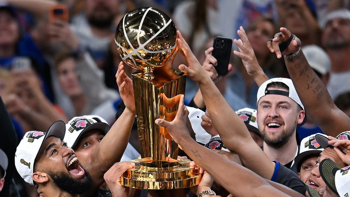 New York Knicks players celebrating with Larry O'Brien Championship Trophy on basketball court.