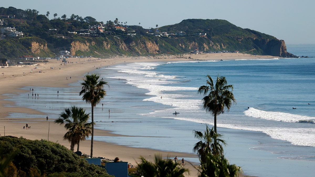 People walking on Zuma Beach with Point Dume in the background in Malibu, California