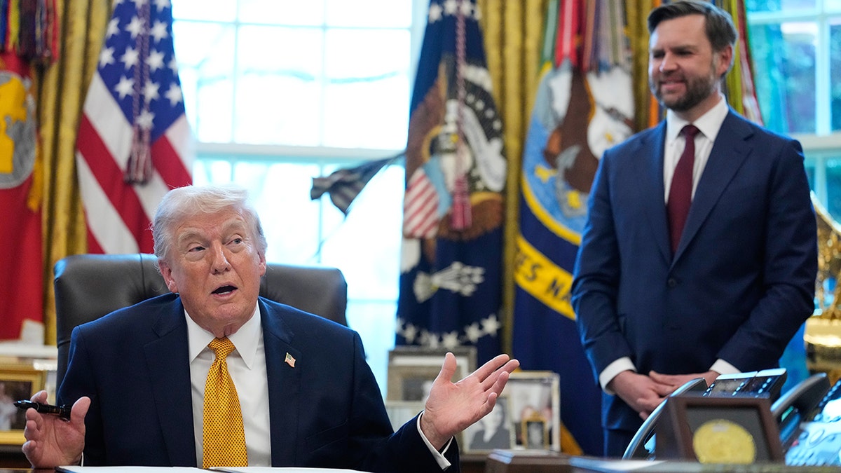 President Donald Trump speaking at his desk in the Oval Office with Vice President JD Vance listening