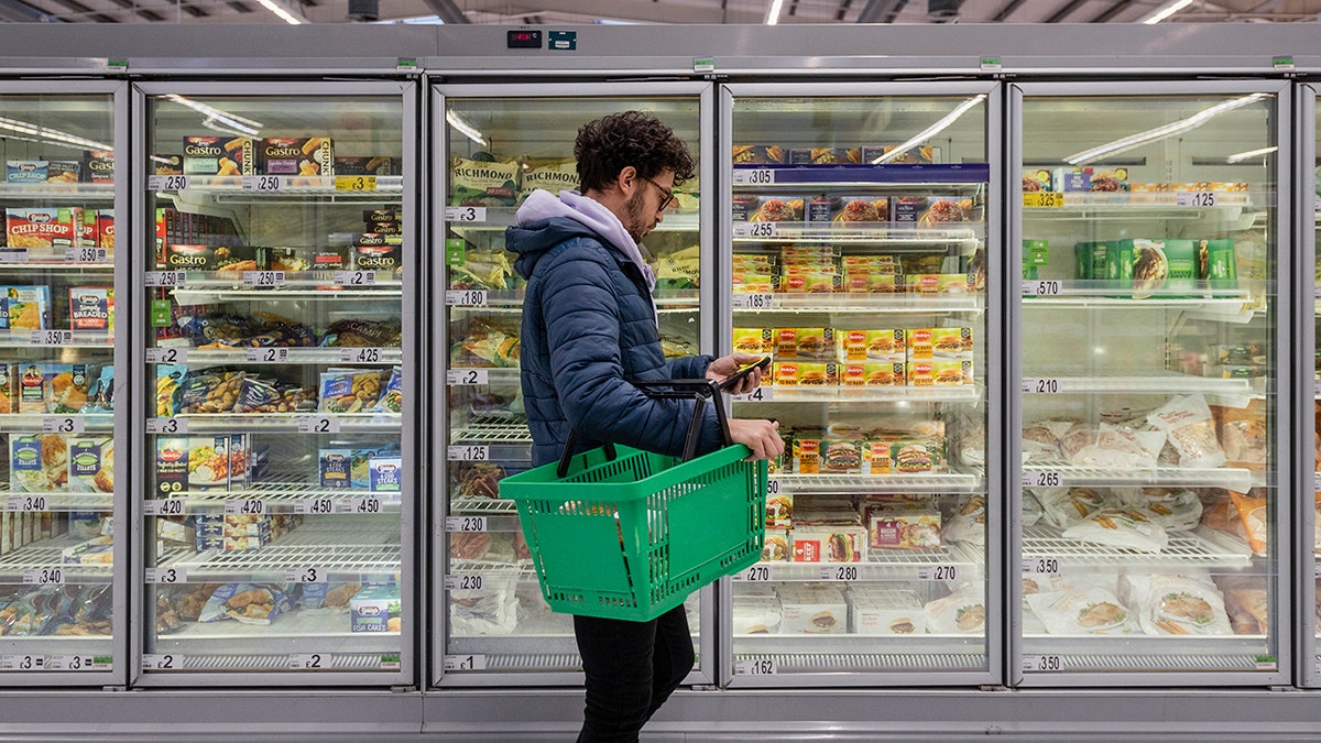 Man standing in front of supermarket freezers looking at his phone