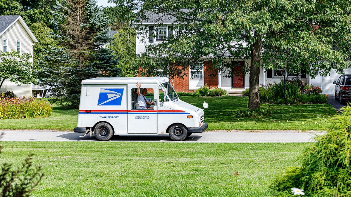 USPS mail carrier waving from a mail delivery van window in a residential neighborhood