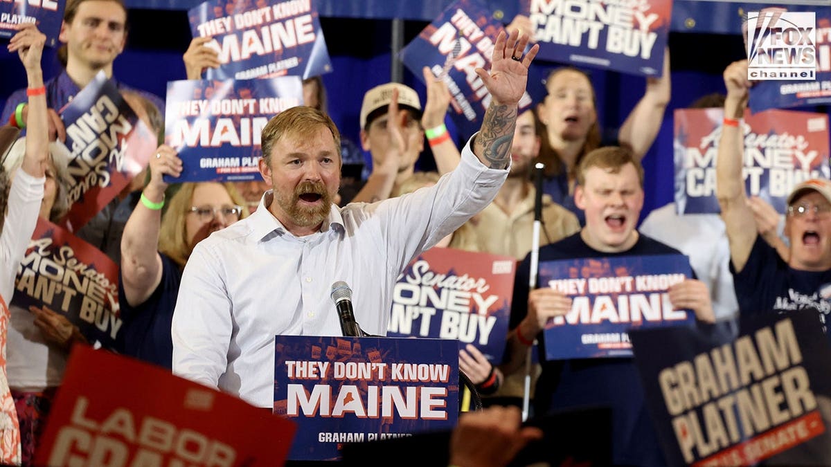 Graham Platner raises his left hand to crowd at his watch party June 9