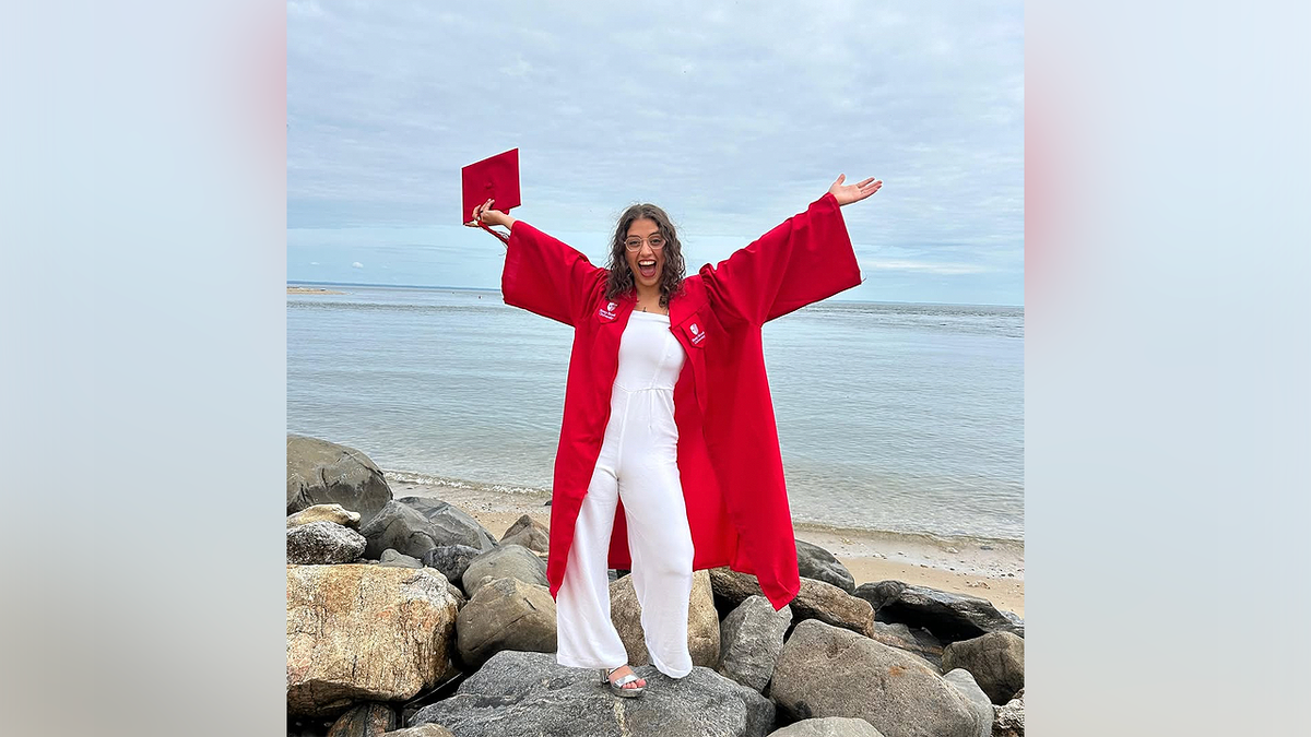 Victoria Castle celebrates graduation while standing on rocks overlooking the water
