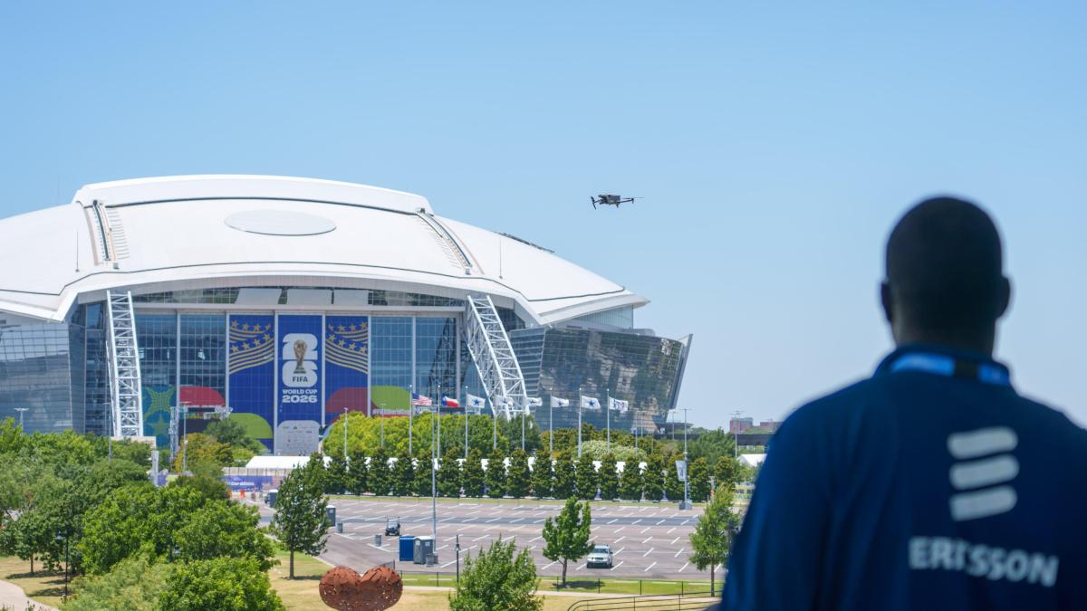 A drone pilot looks out at a drone in the sky in front of a football stadium.