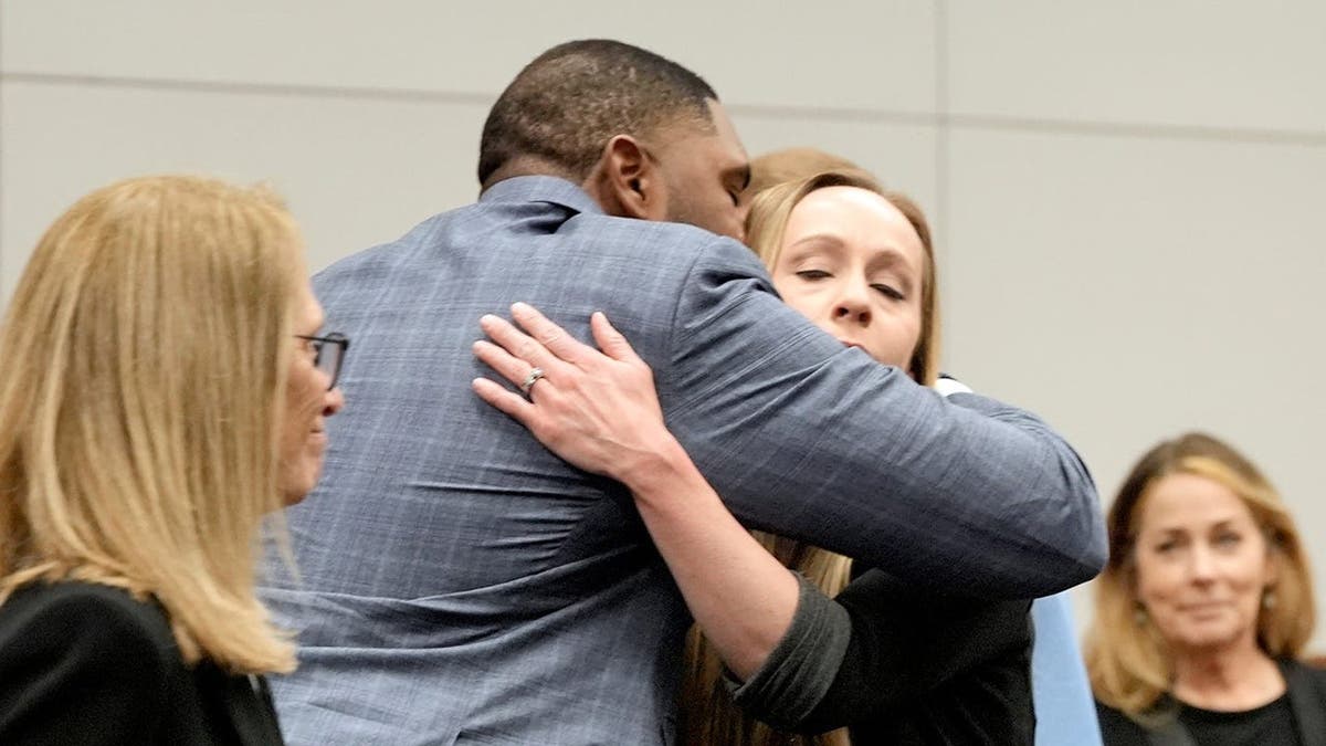 Sherrone Moore and his wife Kelli Moore hug in a courtroom after a ruling.