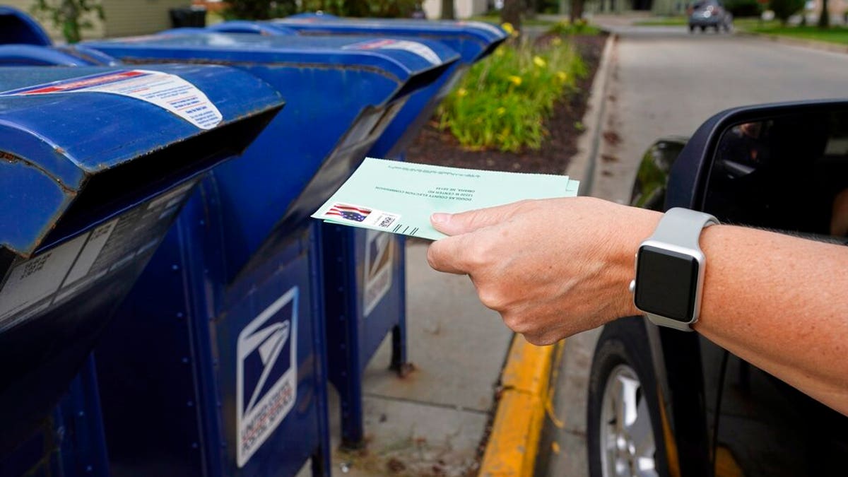 FILE - In this Aug. 18, 2020, file photo, a person drops applications for mail-in-ballots into a mailbox in Omaha, Neb. The U.S. Postal Service agreed Wednesday, Oct. 14, to reverse changes that slowed mail service nationwide, settling a lawsuit filed by Montana Gov. Steve Bullock during a pandemic that is expected to force many more people to vote by mail. (AP Photo/Nati Harnik, File)