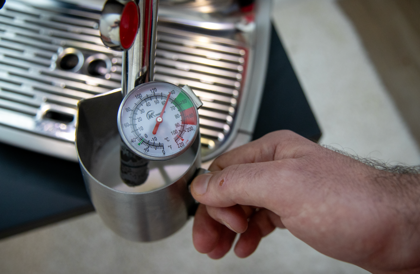 Milk being frothed. A thermometer is being used to gauge the temperature of the milk.