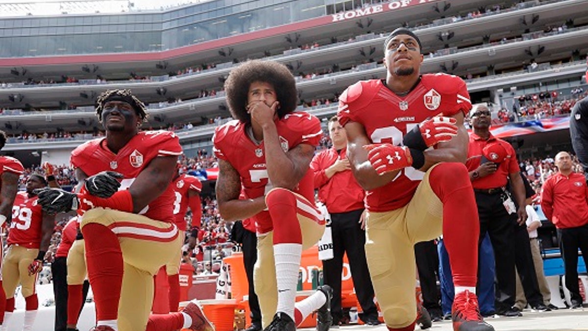 FILE - In this Oct. 2, 2016, file photo, from left, San Francisco 49ers outside linebacker Eli Harold, quarterback Colin Kaepernick, center, and safety Eric Reid kneel during the national anthem before an NFL football game against the Dallas Cowboys in Santa Clara, Calif. What started as a protest against police brutality has mushroomed a year later into a divisive debate over the future of Kaepernick who refused to stand for the national anthem and now faces what his fans see as blackballing for speaking out in a country roiled by racial strife. The once-rising star and Super Bowl quarterback has been unemployed since March, when he opted out of his contract and became a free agent who could sign with any team. (AP Photo/Marcio Jose Sanchez, File)