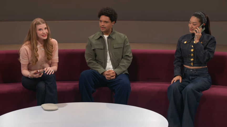 Three people seated on a long couch at a tech event.