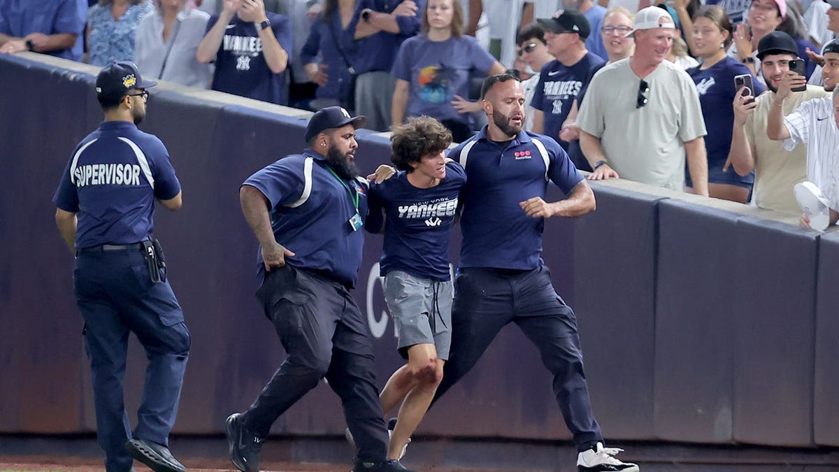 Security escorts a fan off the field during a Yankees-Mariners game at Yankee Stadium.