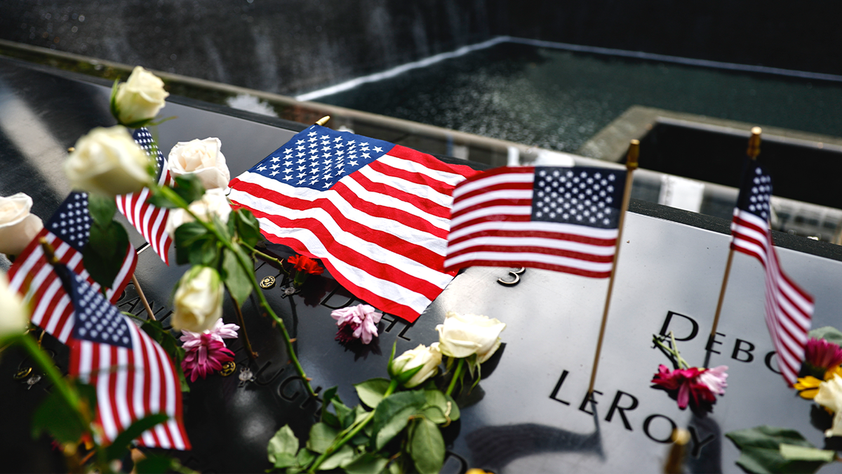 Flowers and American flags rest at 9/11 Memorial reflecting pool.