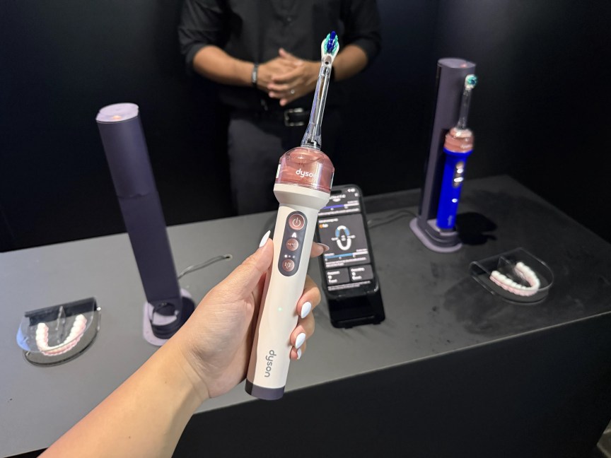 A hand holding the pink Dyson CameraJet toothbrush.